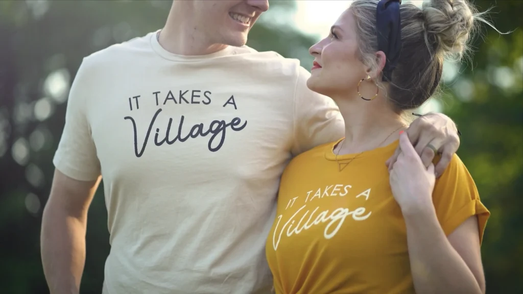 Couple wearing matching “It Takes a Village” shirts during an adoption story film