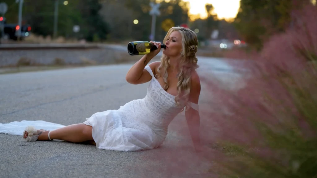 Bride sitting in the street and drinking from a champagne bottle during a wedding portrait session