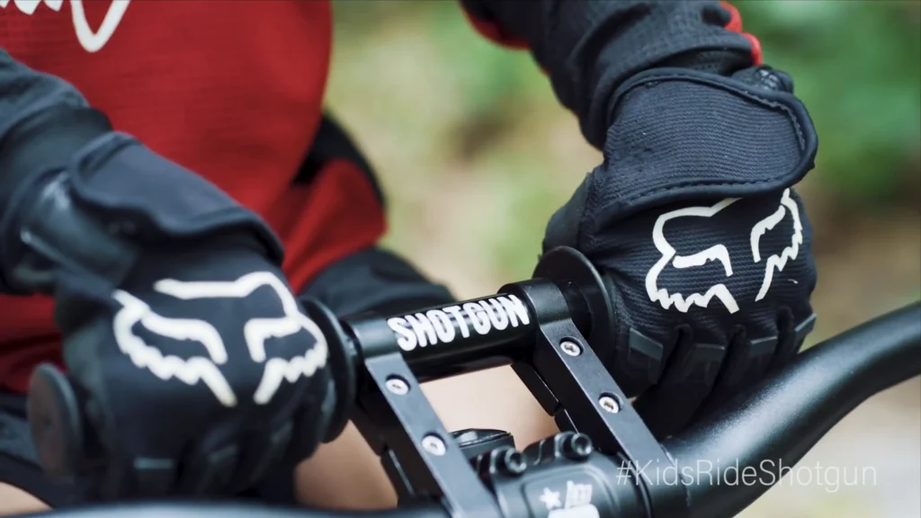 Child gripping a Kids Ride Shotgun handlebar attachment while mountain biking