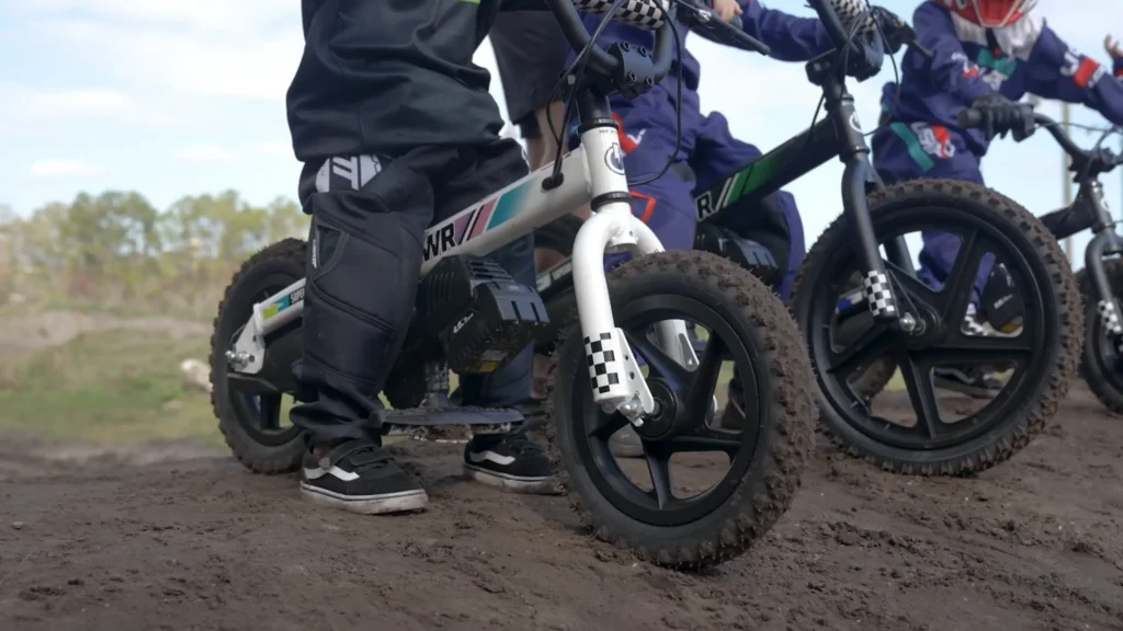 Children riding Superbolt electric balance bikes on a motocross track while learning throttle control and riding fundamentals
